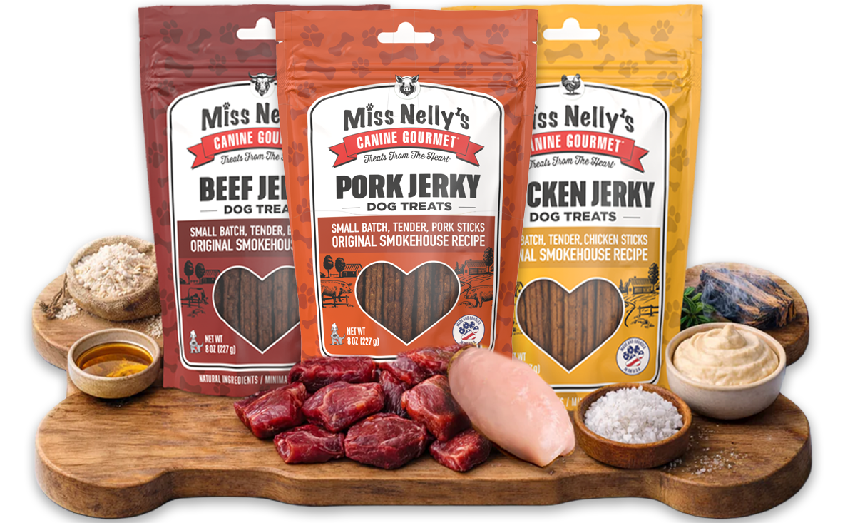 Three packages of Miss Nelly's Gourmet Dog Treats on a wooden board with raw ingredients.